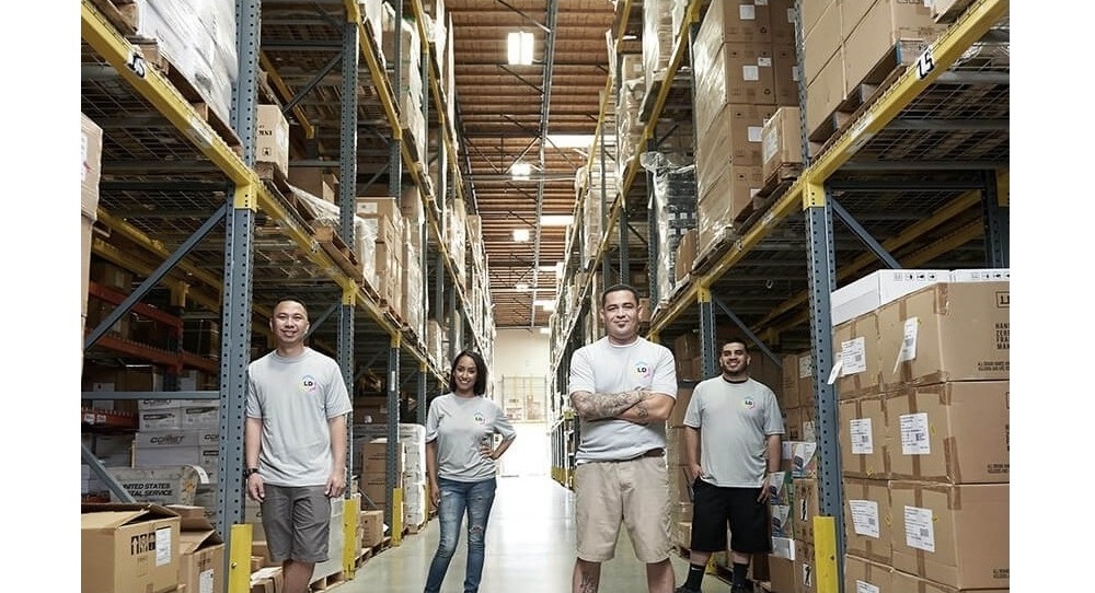 Four employees standing amongst boxes in a warehouse